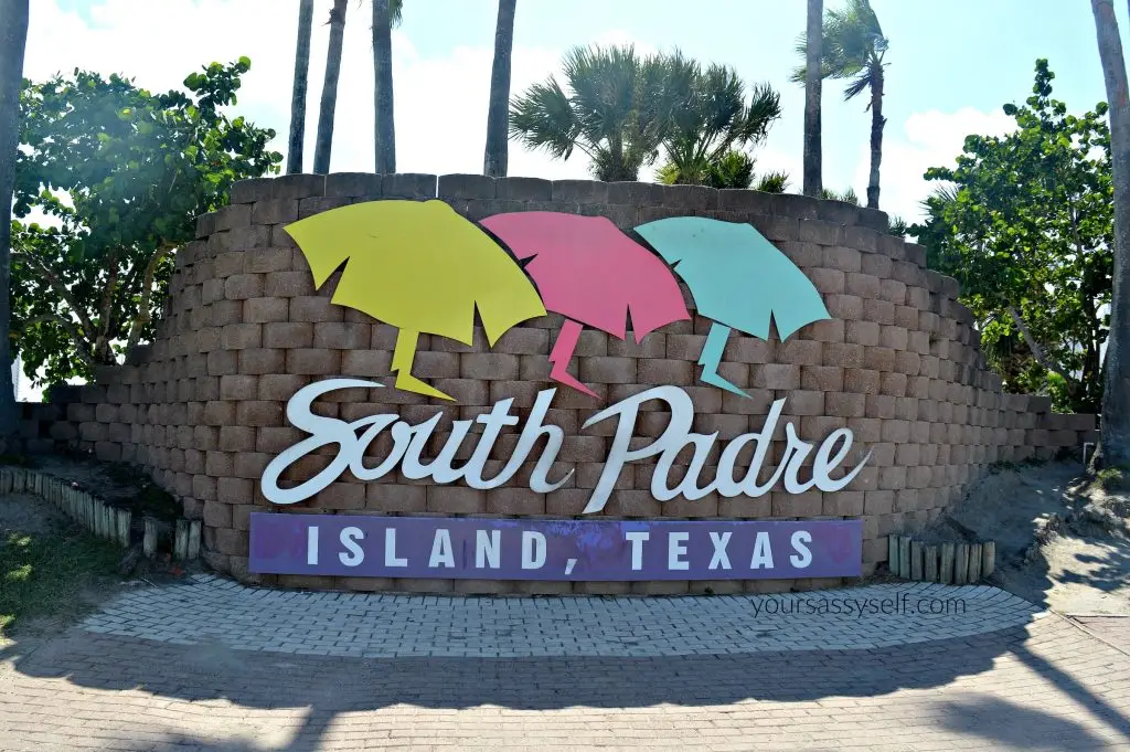 Colorful South Padre Island, Texas welcome sign surrounded by palm trees under a bright blue sky