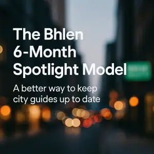 A blurred city street with warm lights in the background. Overlaid white text reads: “The Bhlen 6-Month Spotlight Model — A better way to keep city guides up to date.”